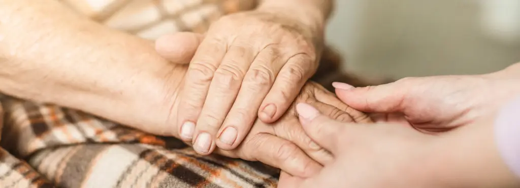 Eine Pflegekraft hält die Hand einer älteren Person in einem warmen, einladenden Raum